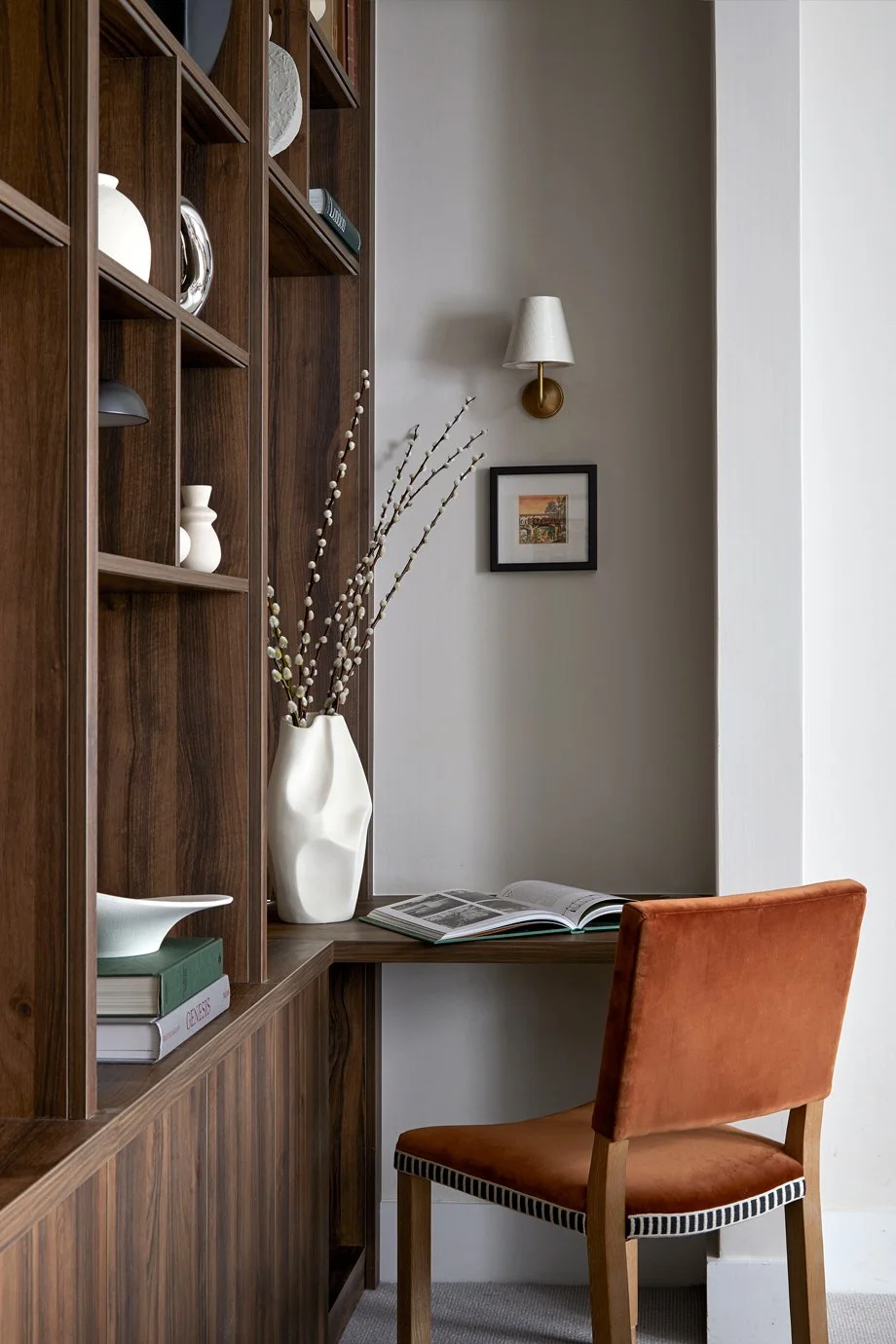An orange chair at a desk integrated into shelving beside a window